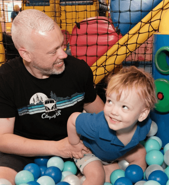 A toddler playing in a colourful ball pit at Jack in the Box Club, with their dad holding them, sharing a fun and engaging moment together.