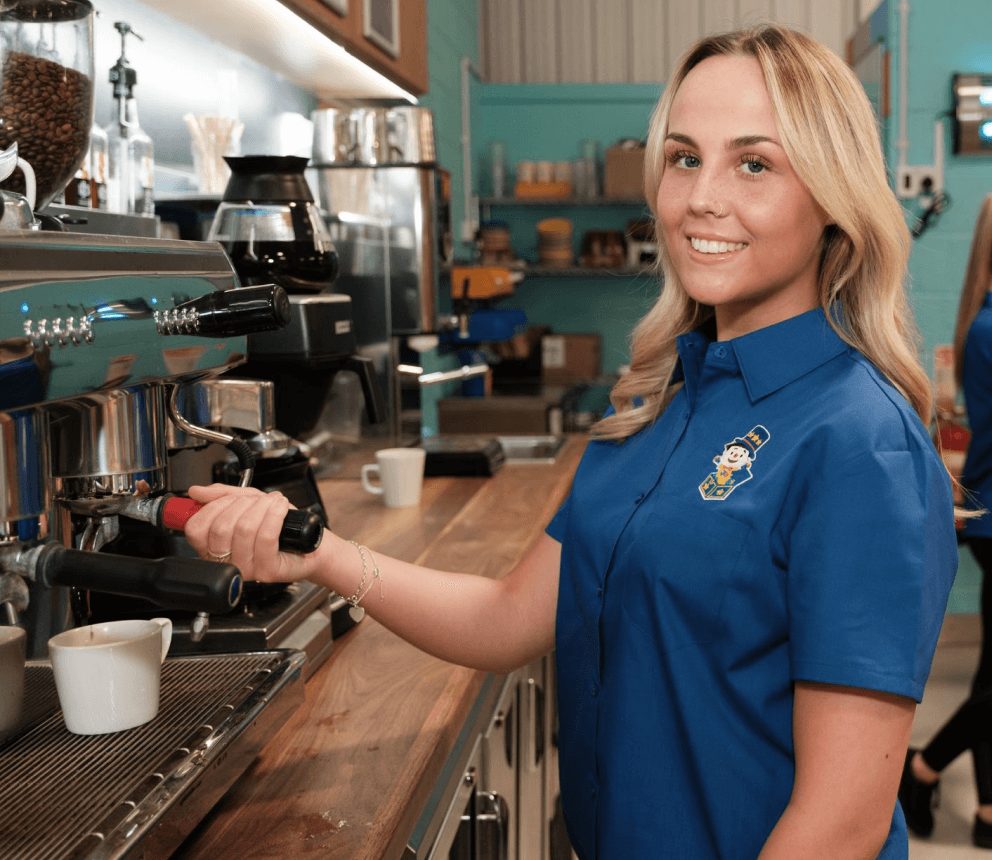 A friendly staff member serving a freshly brewed coffee at the Soft Play Cafe, offering a warm welcome to visitors and parents.