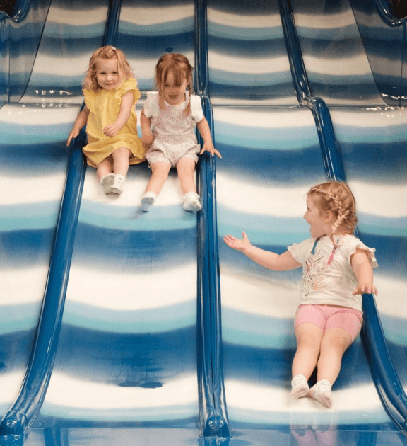 A little girl going down a soft play slide with her friends at Jack in the Box Club, smiling and enjoying a fun and exciting moment in the play area.