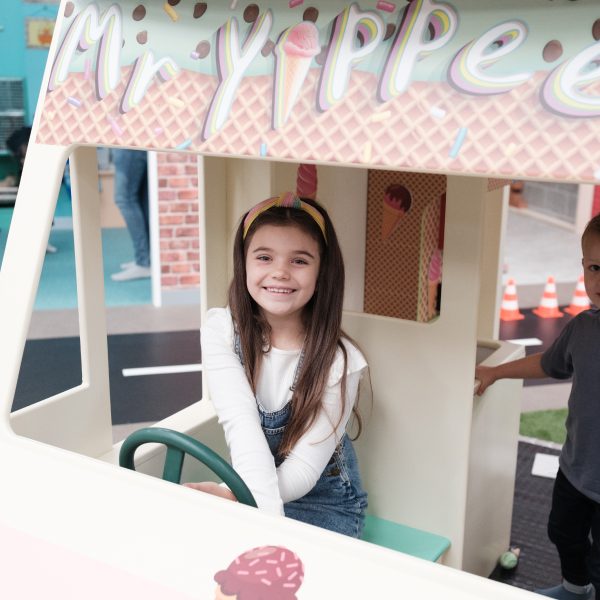 A little girl playing with the pretend ice cream set in the role-play area at Jack in the Box Club, pretending to drive the Mr Yippee van.