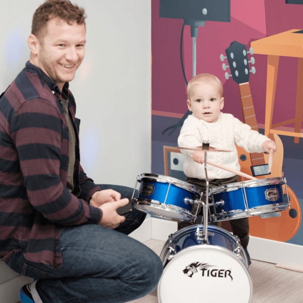 A baby playing with drums at Jack in the Box Club, enjoying a fun and interactive music experience in a playful environment.