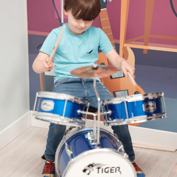 A boy in the role-play music area at Jack in the Box Club, playing a drums and enjoying a fun, interactive musical experience.