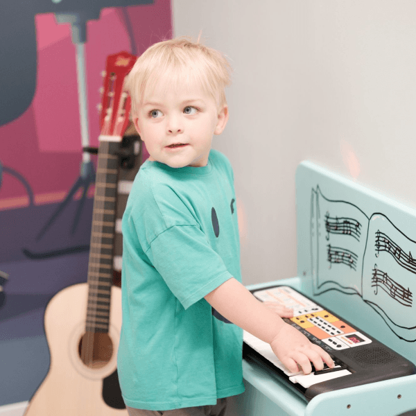 A boy in the role-play music area at Jack in the Box Club, playing a keyboard and enjoying a fun, interactive musical experience.
