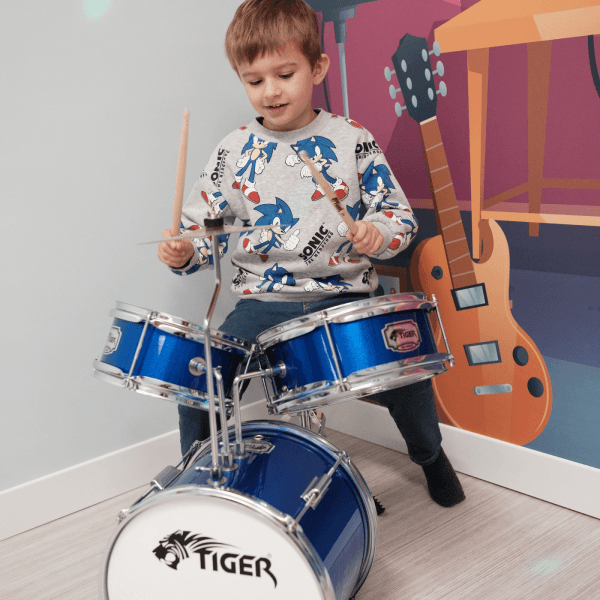 A boy in the role-play music area at Jack in the Box Club, playing a drums and enjoying a fun, interactive musical experience.